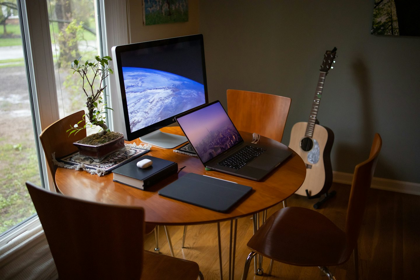 Wooden desk with monitor, laptop, bonsai, and drawing tablet.
